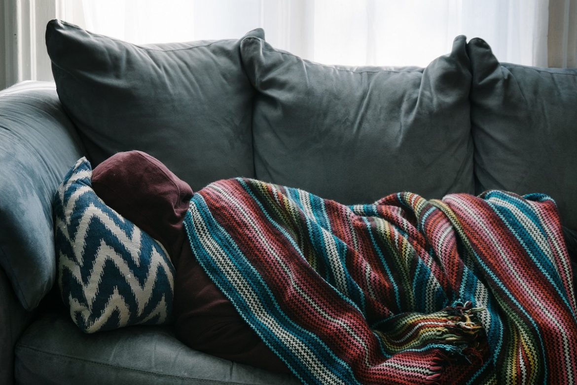 Человек на диване, спит, завернувшись в одеяло, натянув на голову капюшон